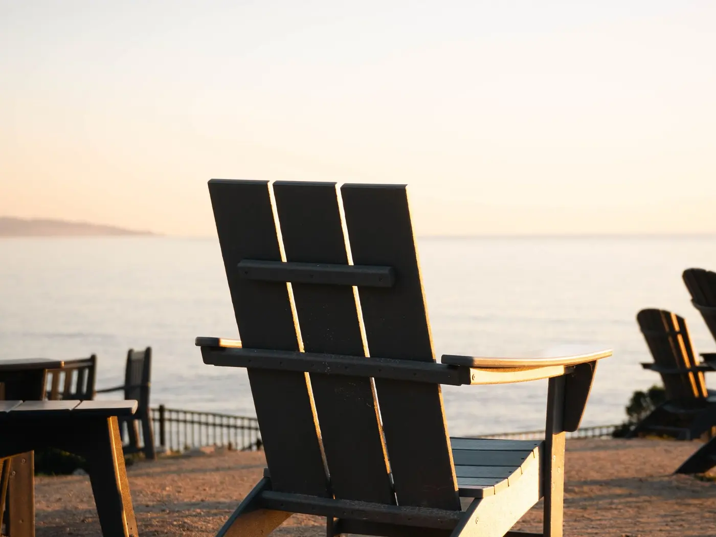 An empty Adirondack chair facing the ocean at sunset
